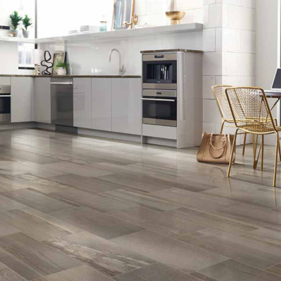 Modern kitchen with polished wood-look tile flooring in muted browns and grays, sleek light gray cabinetry, dark countertops, and a small dining area with golden wire-mesh chairs.